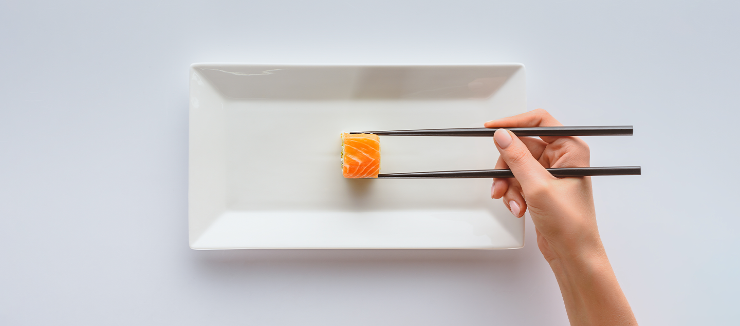 Observamos a una personas aprendiendo a usar palillos chinos mientras disfrutan de un sushi.